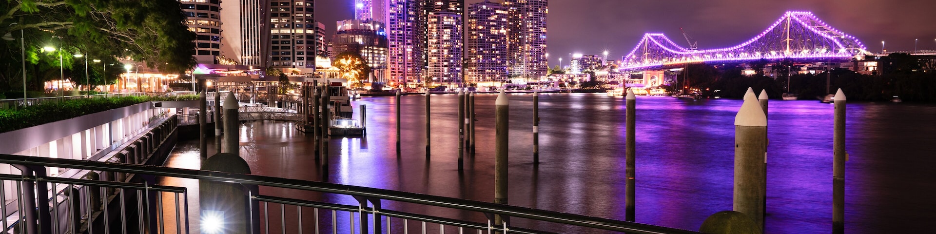 Un paisaje urbano nocturno con rascacielos iluminados y un puente con luces púrpuras.