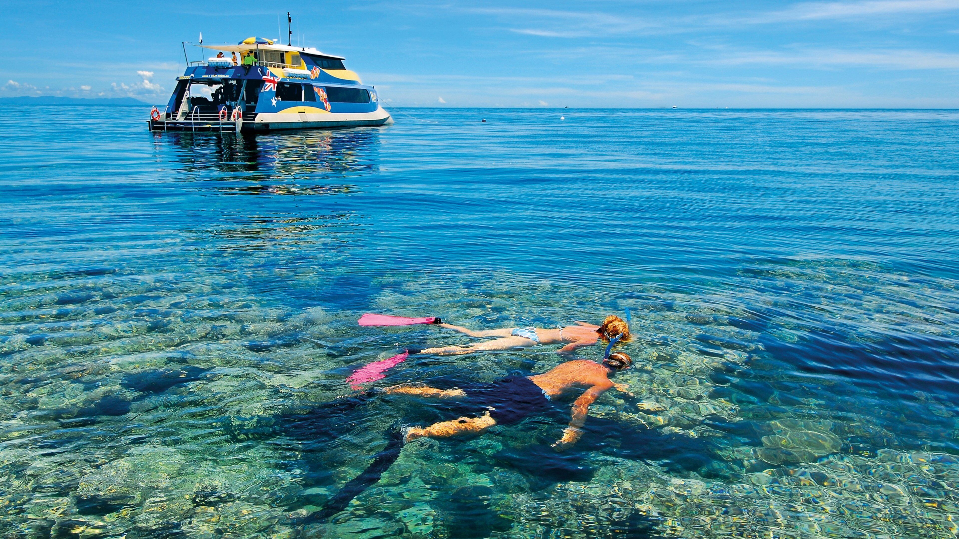 A person swimming in clear blue water with a boat in the background.