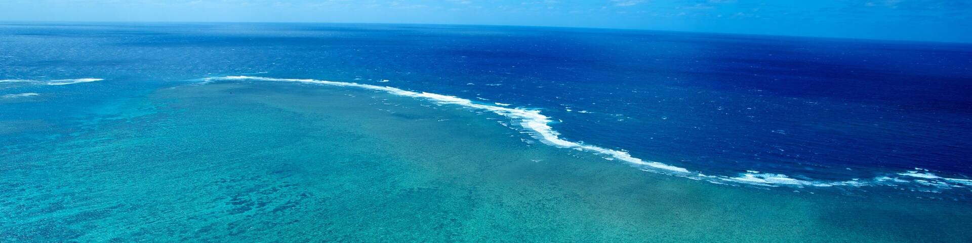A clear blue ocean with a sandy beach and a coral reef.