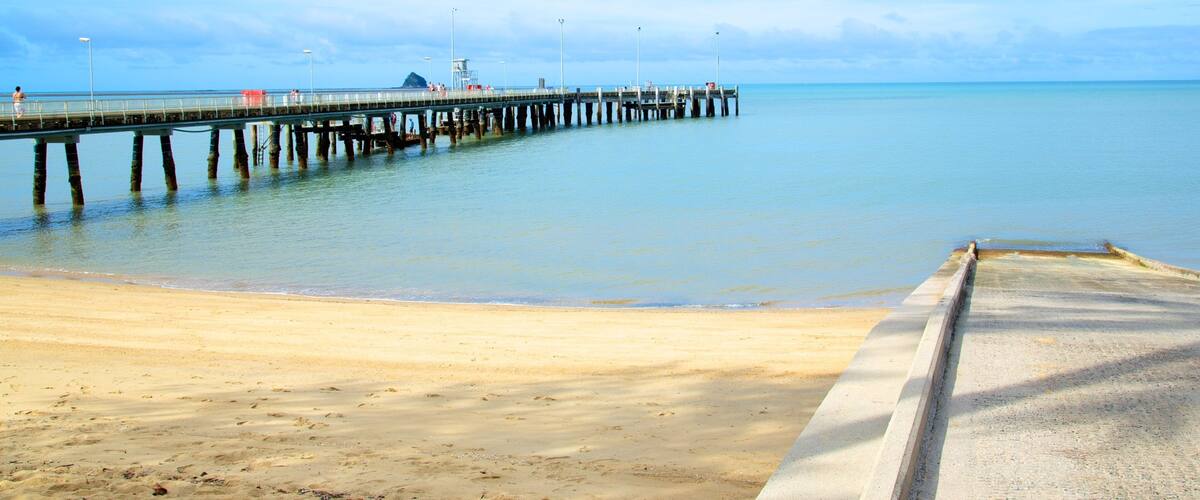 A beach with a pier extending into calm waters.
