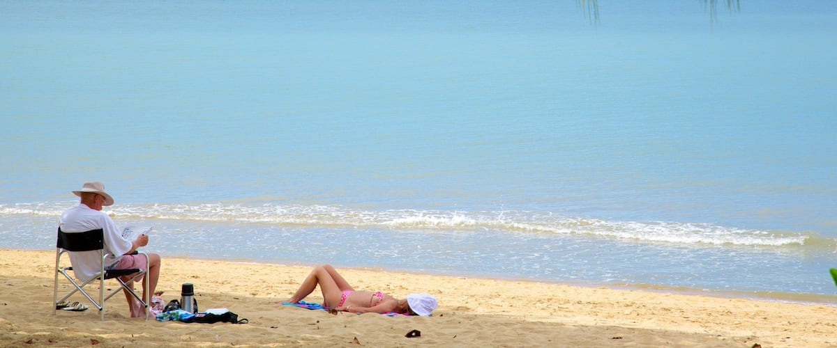 A beach with a man reading a book and a woman sunbathing.