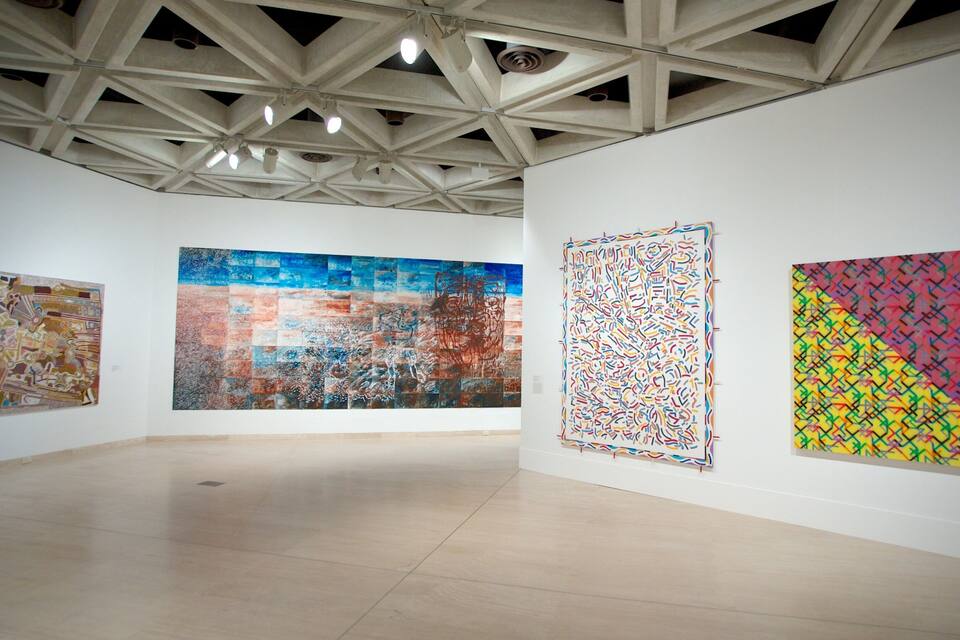 Een kunstgalerie met drie grote abstracte schilderijen aan de muur.