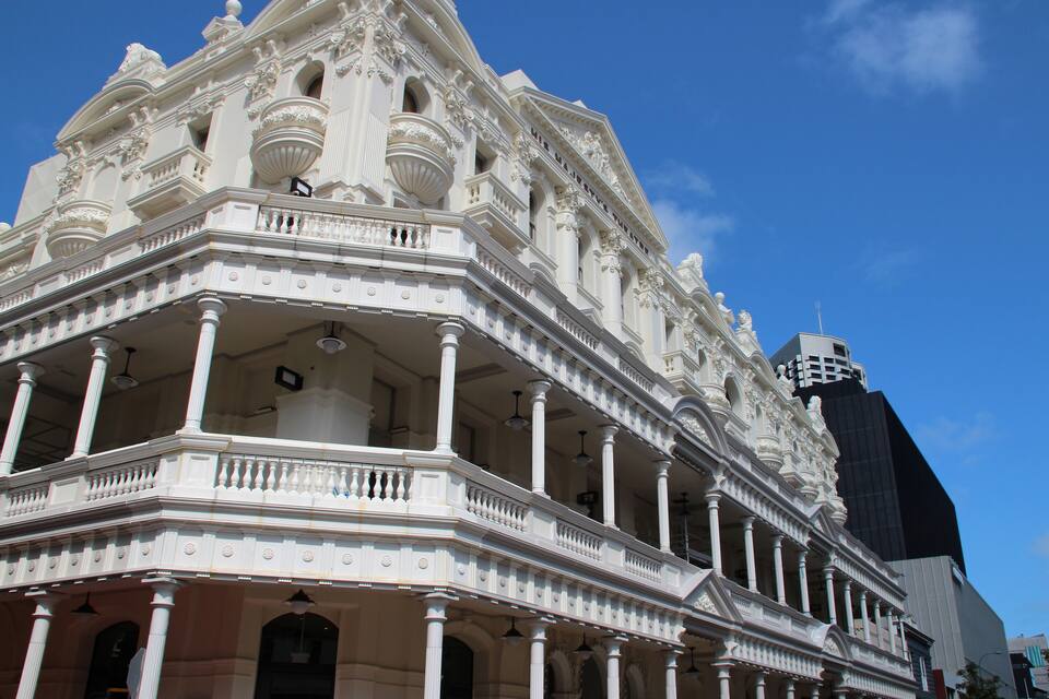 Un bâtiment blanc, richement décoré, avec des colonnes et des balcons, se dressant sur un ciel bleu clair.