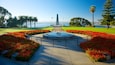A memorial with a cross, surrounded by red flowers and palm trees.