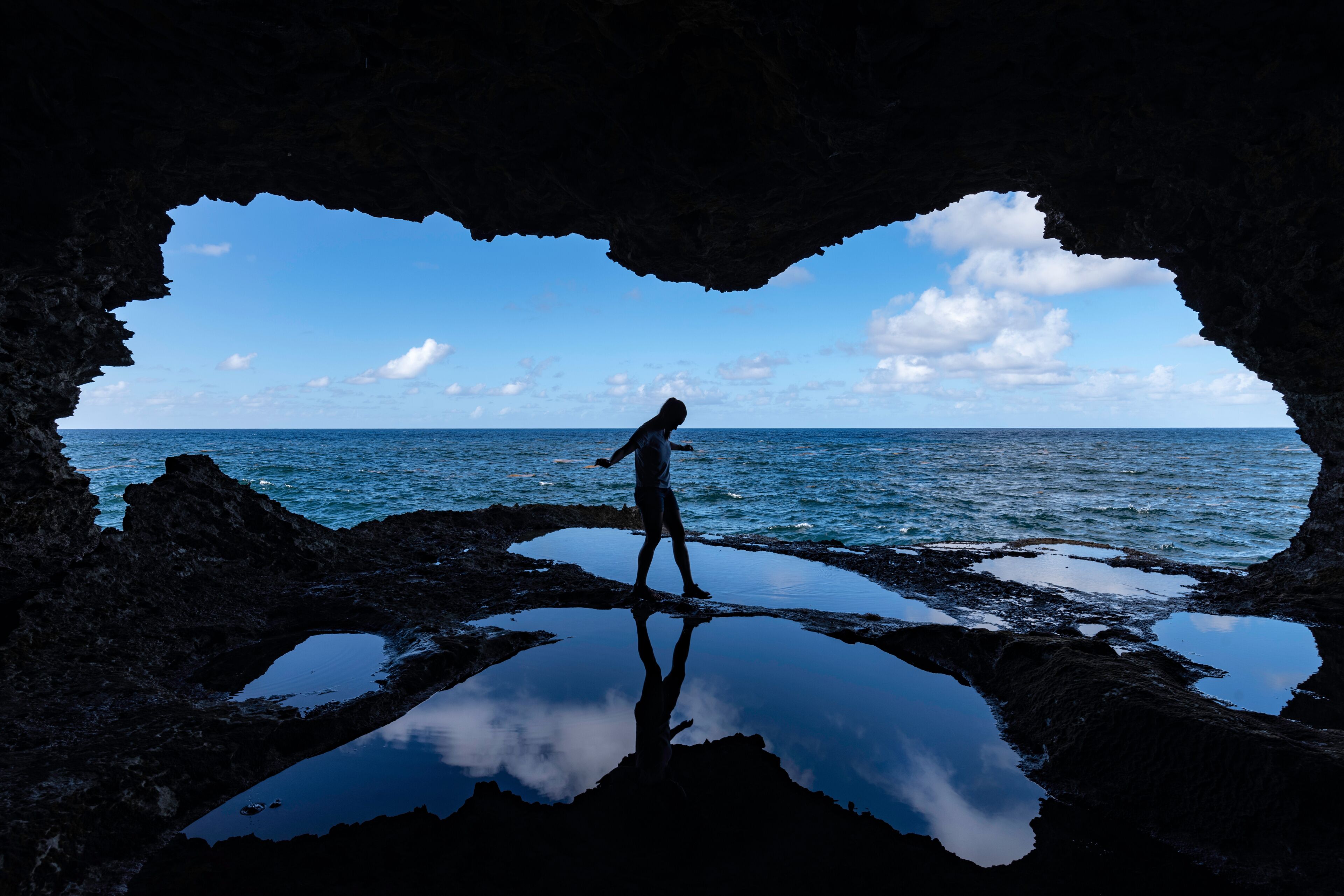 A person standing in a cave with a view of the ocean.