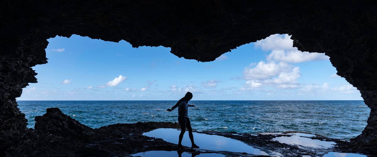 A person standing in a cave with a view of the ocean.