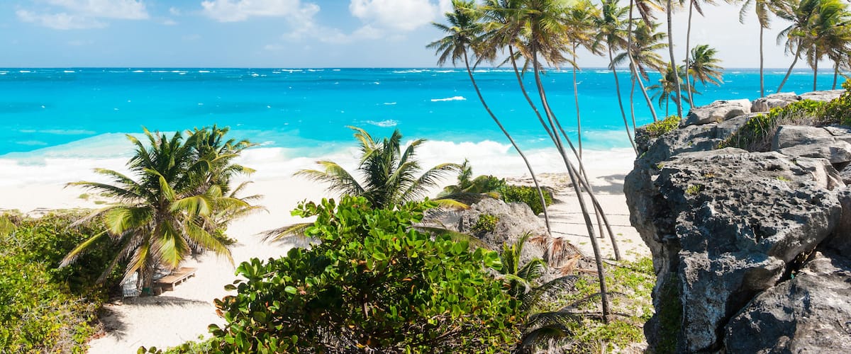 A tropical beach with clear blue water, palm trees, and rocky outcrops.