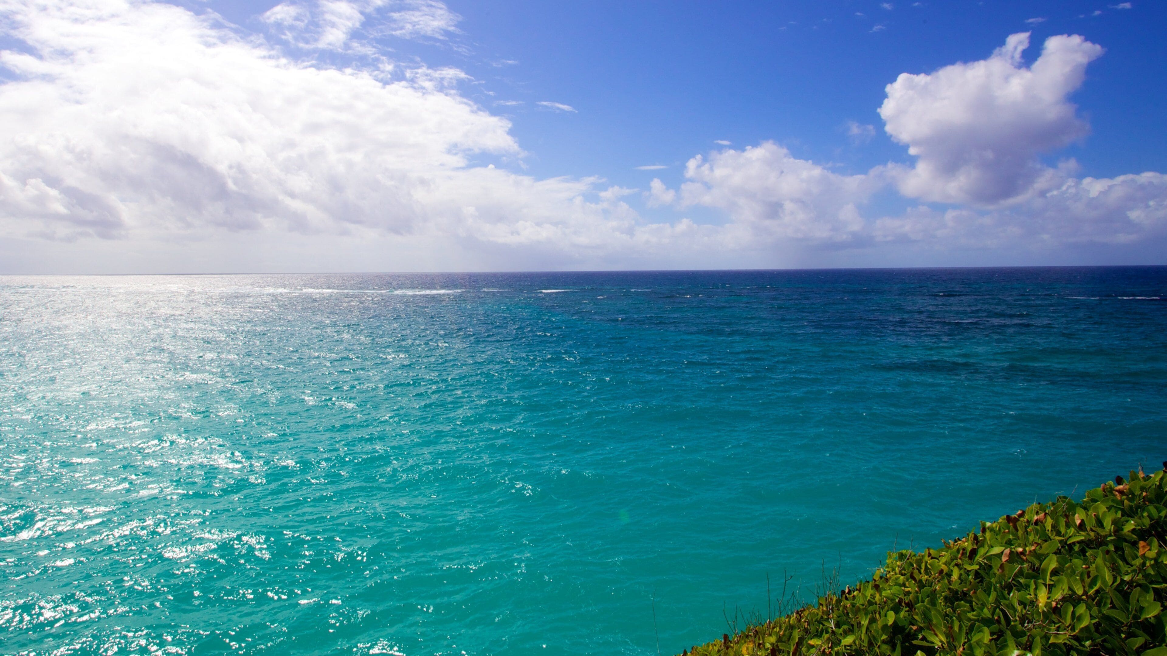 A turquoise ocean with a clear sky and scattered clouds.