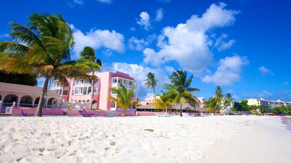 A beach with white sand, palm trees, and pink buildings.