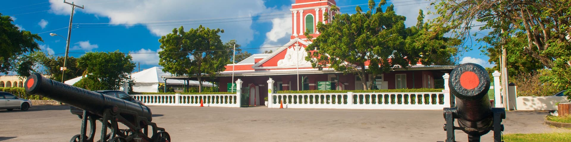 A church with a clock tower, two cannons, and a clear blue sky.