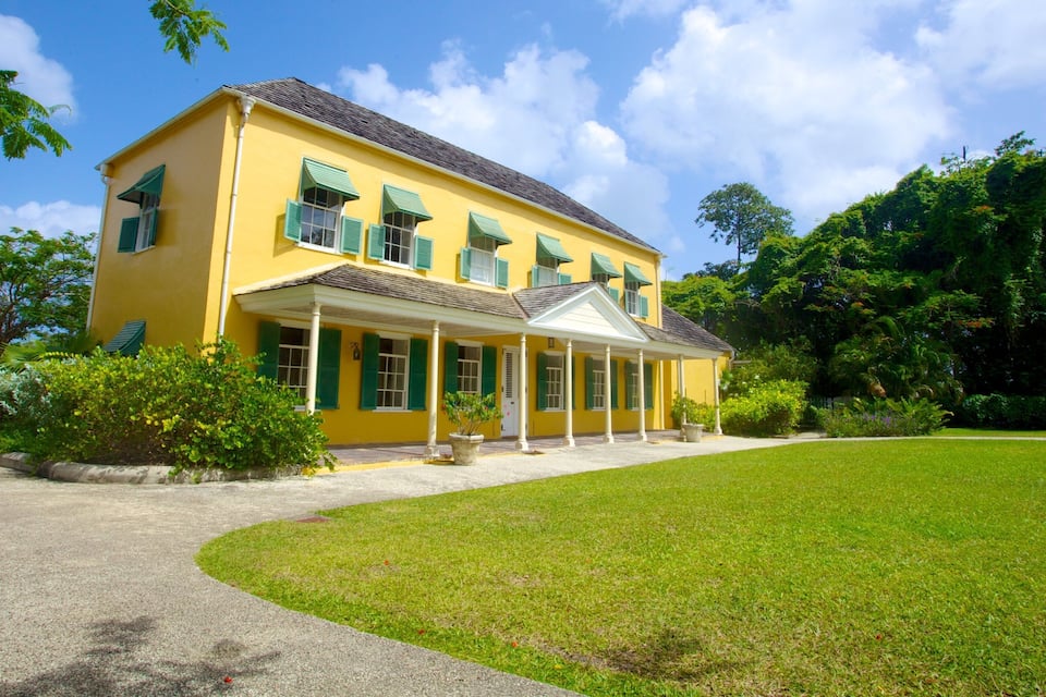 A yellow building with green shutters, surrounded by a well-maintained lawn and trees.