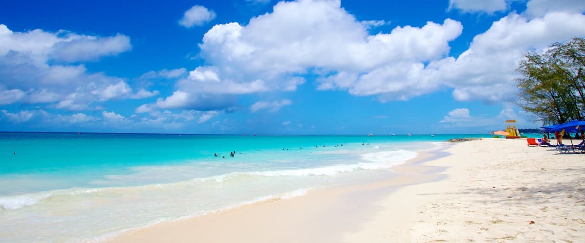 A beach with clear turquoise water, white sand, and a few people swimming.