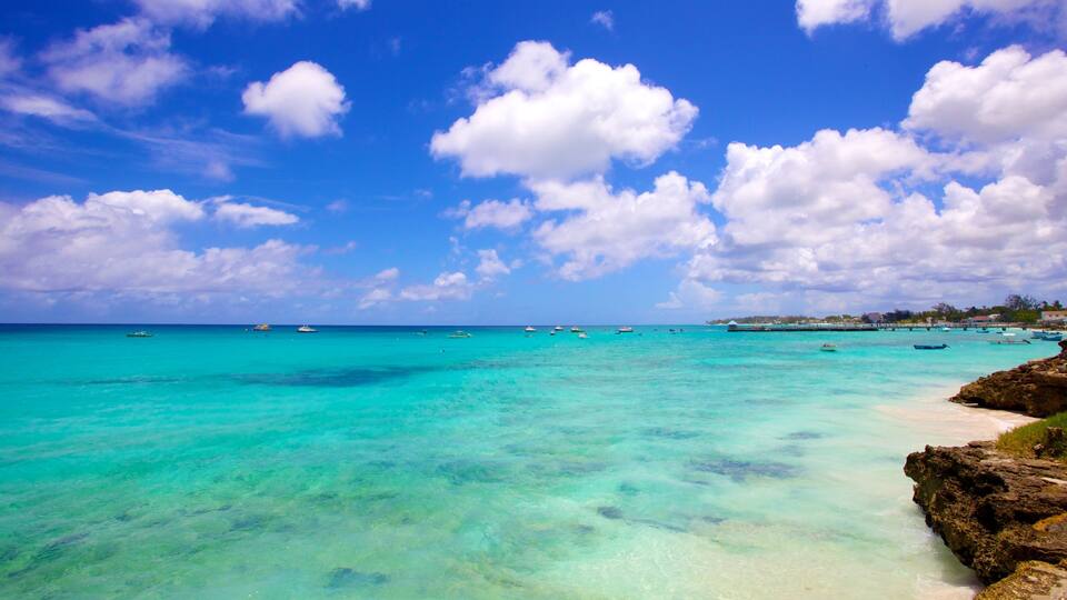 A turquoise sea with boats, a clear sky, and rocky coastline.