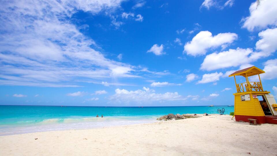 A beach with clear turquoise water, a yellow lifeguard tower, and a clear blue sky with scattered clouds.