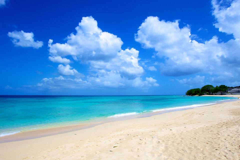 Una playa con agua turquesa, orilla arenosa y nubes dispersas.