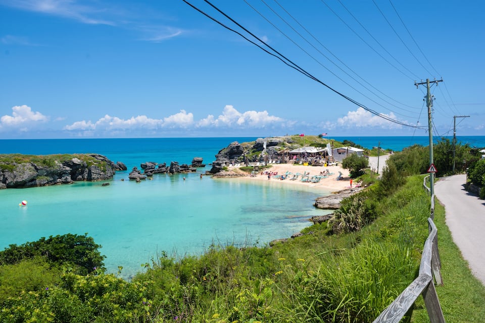 A coastal landscape with clear turquoise waters, a sandy beach, and a road curving along the shore.