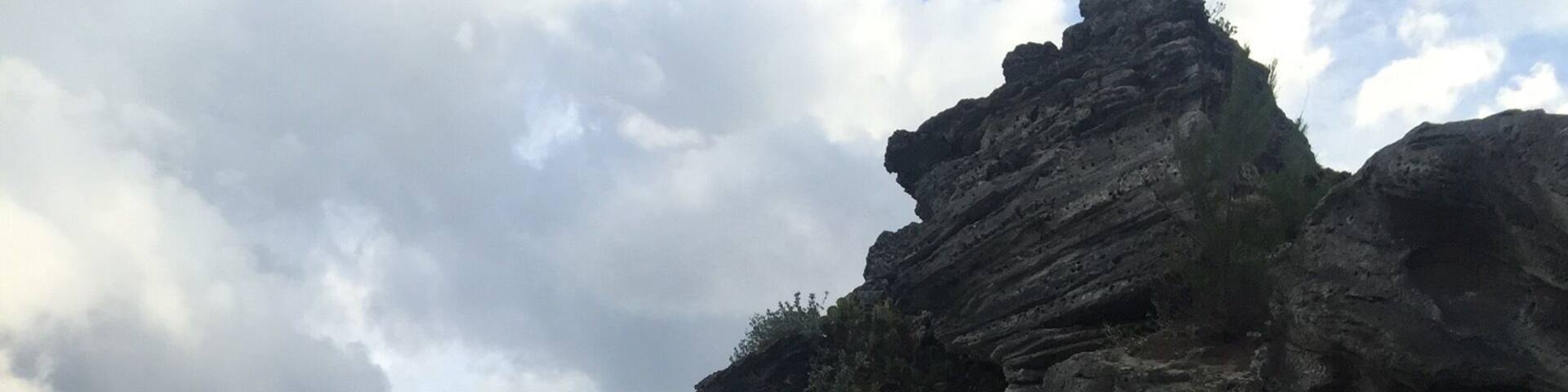 A rocky cliff by a beach with clear turquoise water.
