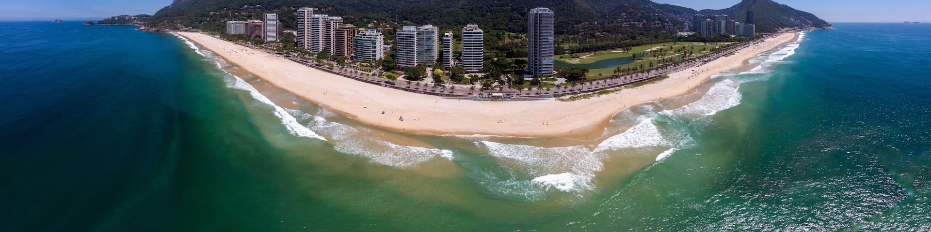 A coastal cityscape with a prominent mountain range, a beach, and high-rise buildings.