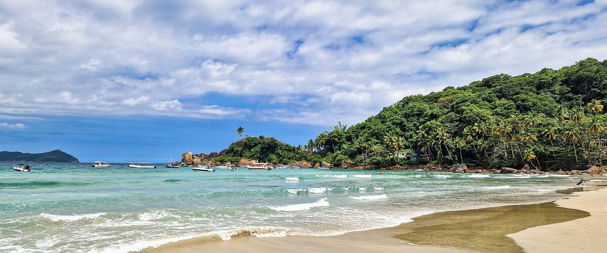 A beach with clear turquoise water, a sandy shore, and lush green hills in the background.