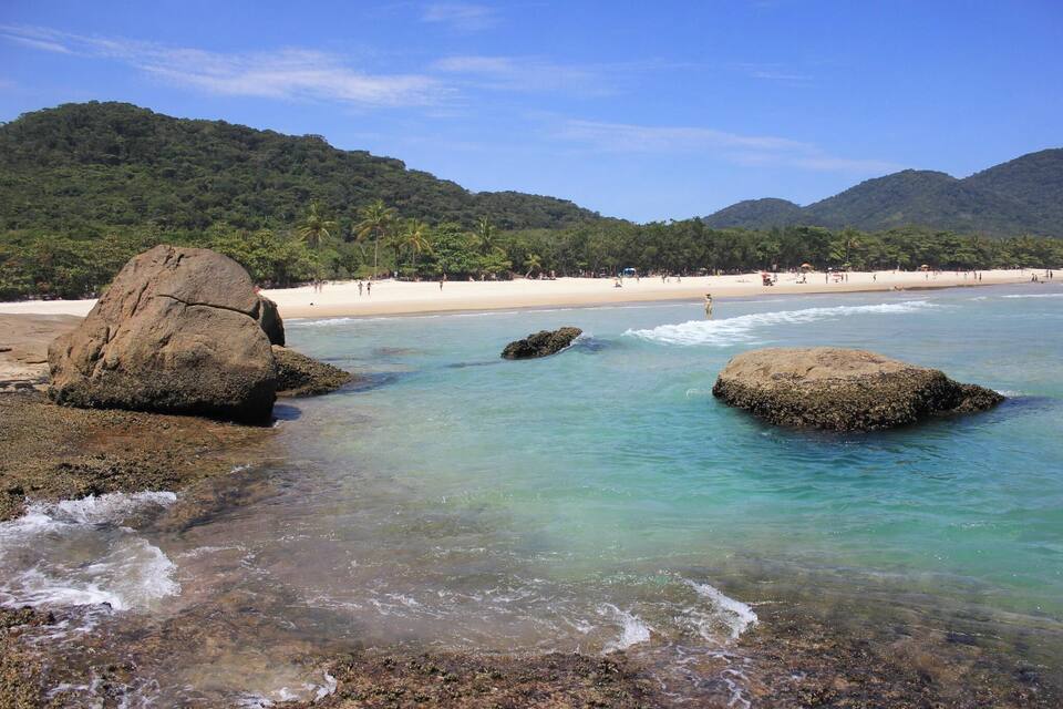A beach with clear turquoise water, large rocks, and a sandy shore.
