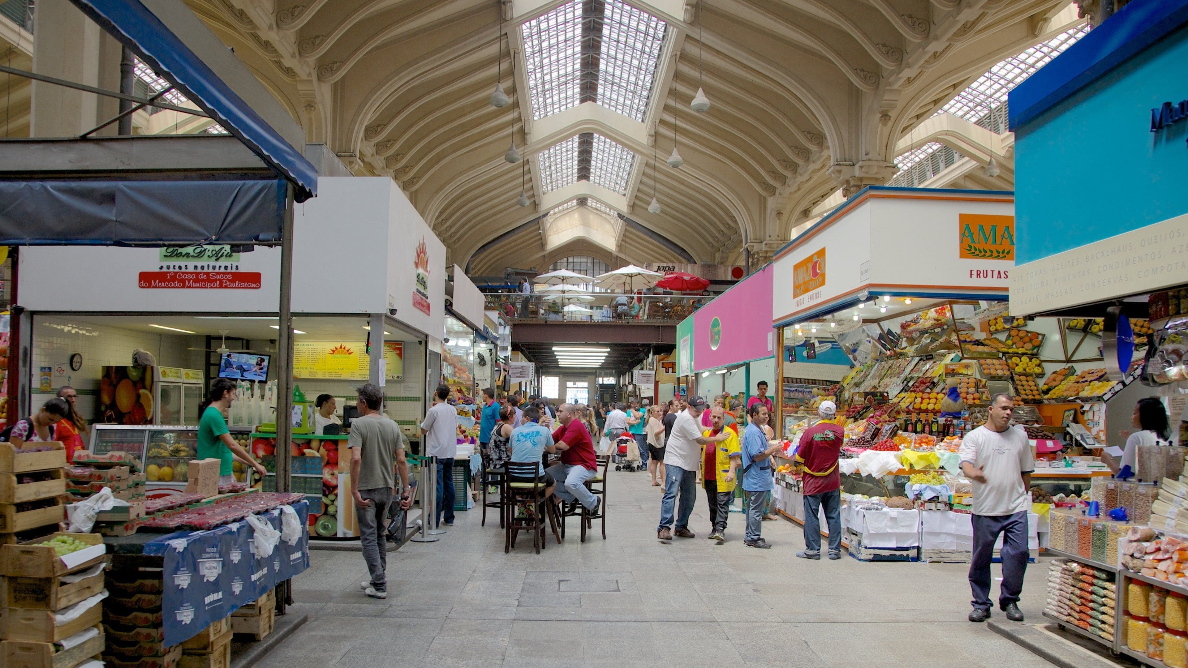 Een overdekte markt met hoge plafonds, diverse kraampjes met fruit en groenten, en mensen die winkelen.