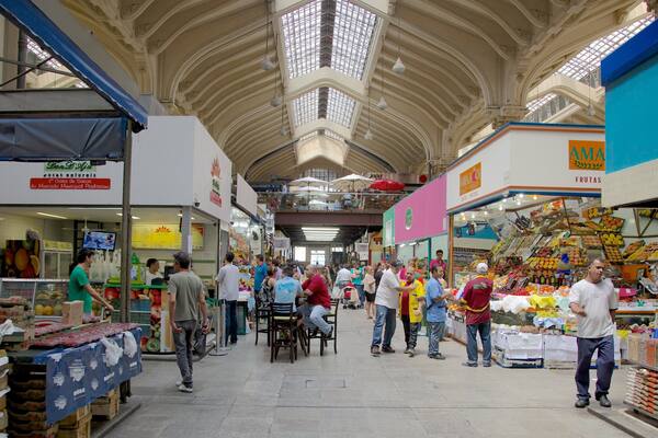 Un marché couvert avec de hauts plafonds, divers étals vendant des fruits et des légumes, et des gens qui font leurs courses.