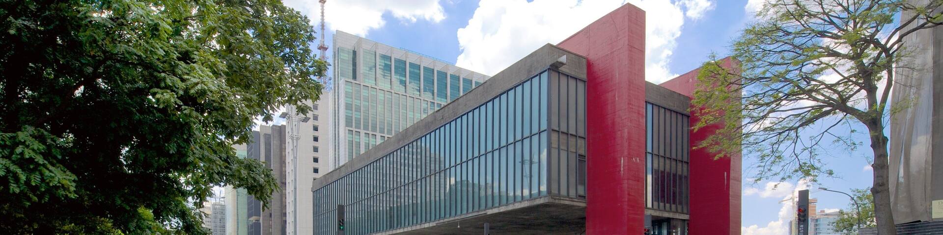 Un edificio moderno con grandes ventanales y detalles en rojo, rodeado de árboles y calles concurridas.