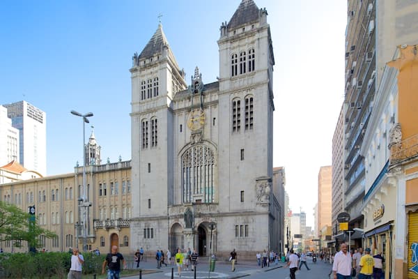 Une cathédrale historique, dotée de deux tours jumelles et d’une grande horloge, entourée de bâtiments modernes et de piétons.