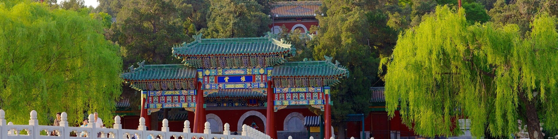 A traditional Chinese temple with a large white stupa, surrounded by lush greenery and a red-roofed pavilion.