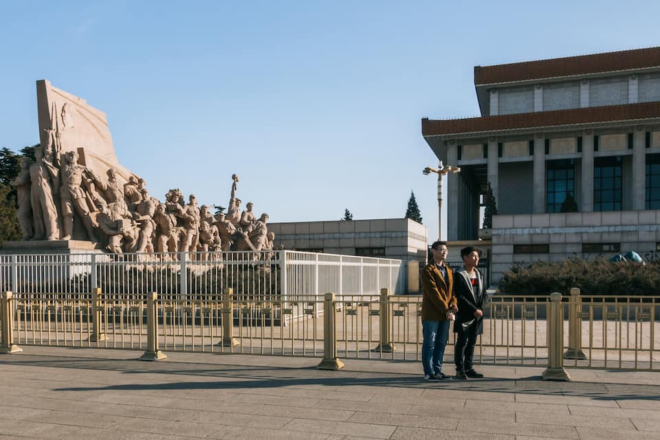 Grande escultura ao ar livre de soldados em uma área cercada, com um edifício moderno ao fundo.