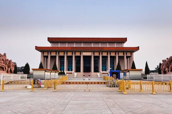 A large building with a red roof and columns, flanked by two large statues.