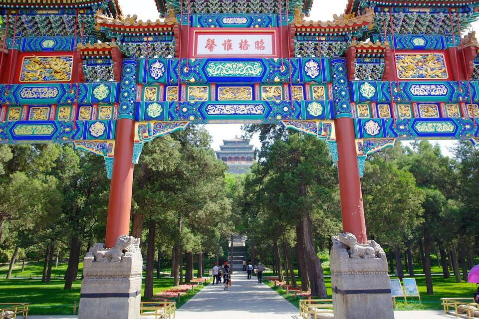 A traditional Chinese gate with intricate blue and gold designs, flanked by stone lion statues, leading to a distant pagoda.