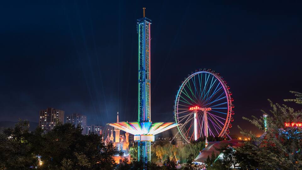A brightly lit Ferris wheel and a tall tower with a unique roof structure.
