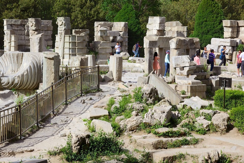 Ancient ruins with stone columns and a metal fence.