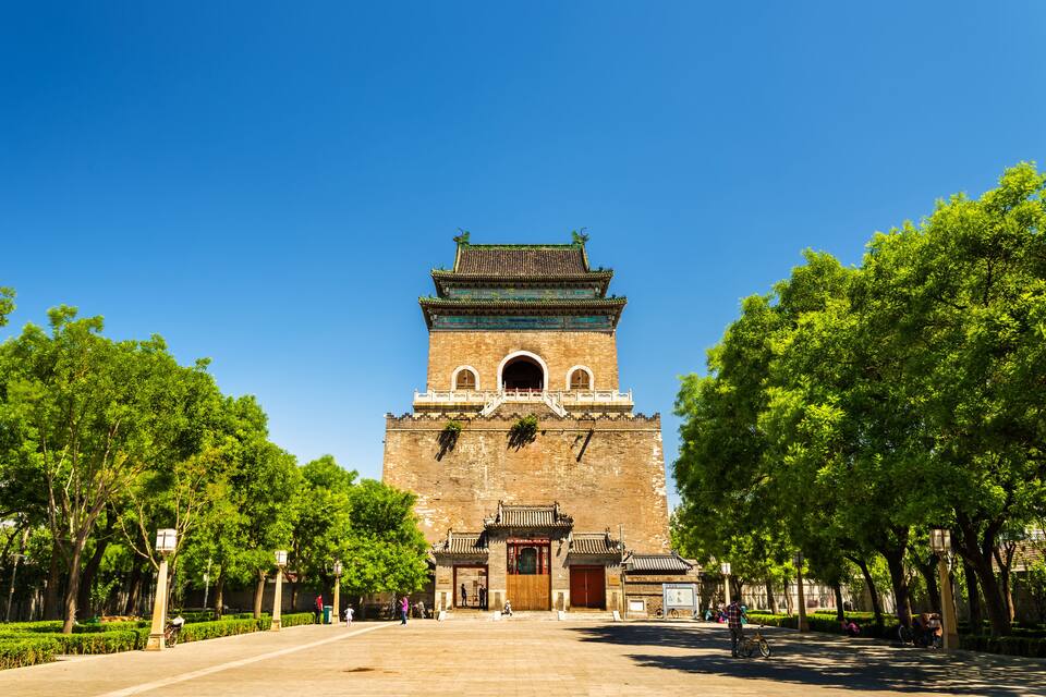 A historic tower with traditional architecture, surrounded by lush green trees and a clear blue sky.