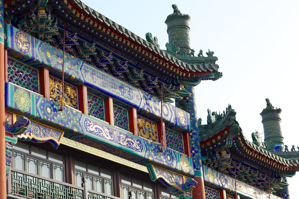 Um edifício tradicional chinês com ornamentação azul e dourada requintada, pilares vermelhos e desenhos complexos no telhado.
