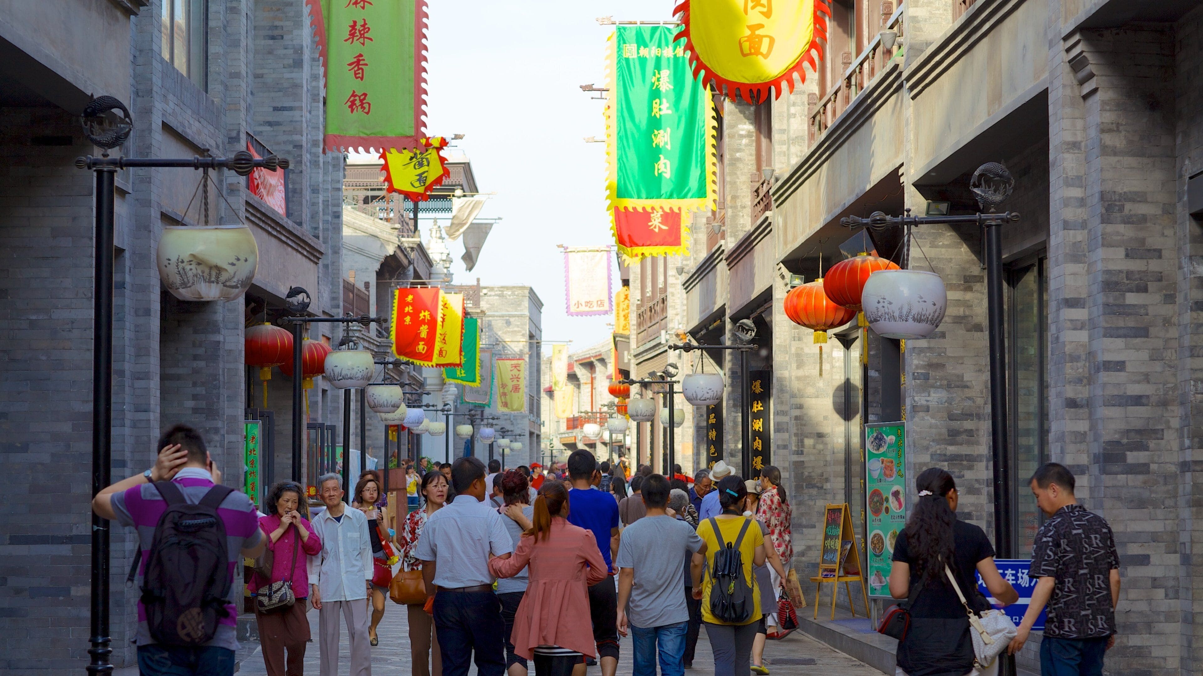 A crowded street with traditional architecture, hanging lanterns, and various colorful banners.