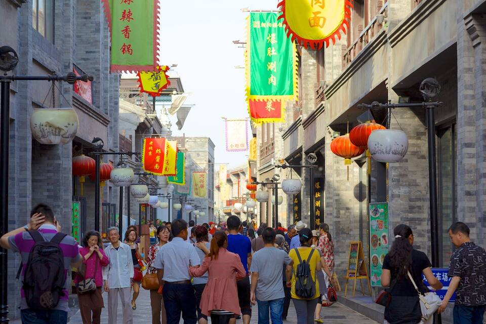 A crowded street with traditional architecture, hanging lanterns, and various colorful banners.
