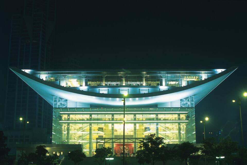 Un edificio moderno con techo curvo y fachada de vidrio por la noche.