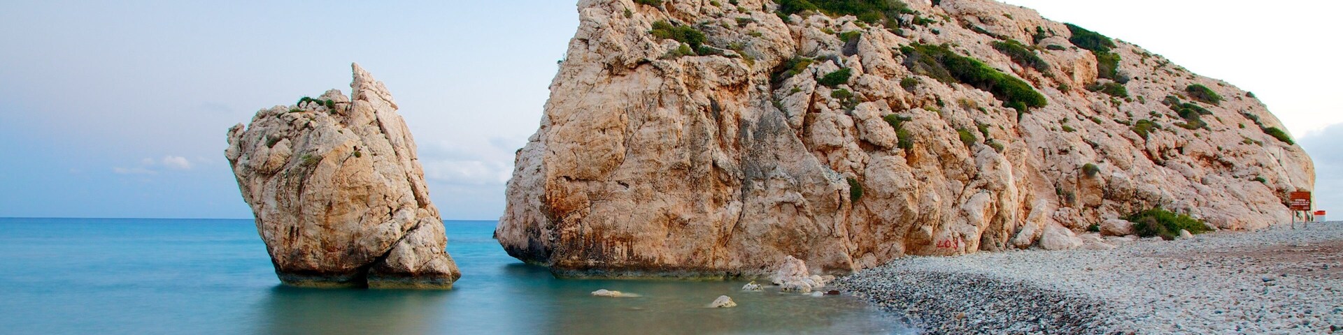 A rocky coastline with a large rock formation and a smaller rock in the water.