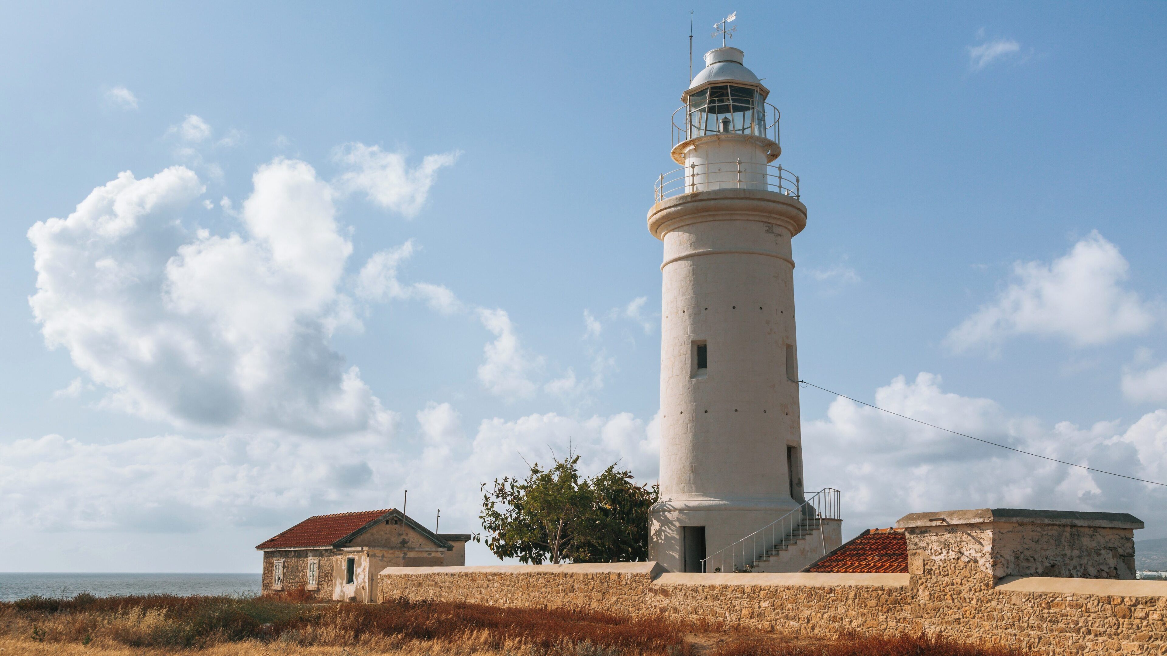 Tall lighthouse standing near the coast of Paphos Archaeological Park with cloudy sky and sea views in Cyprus
