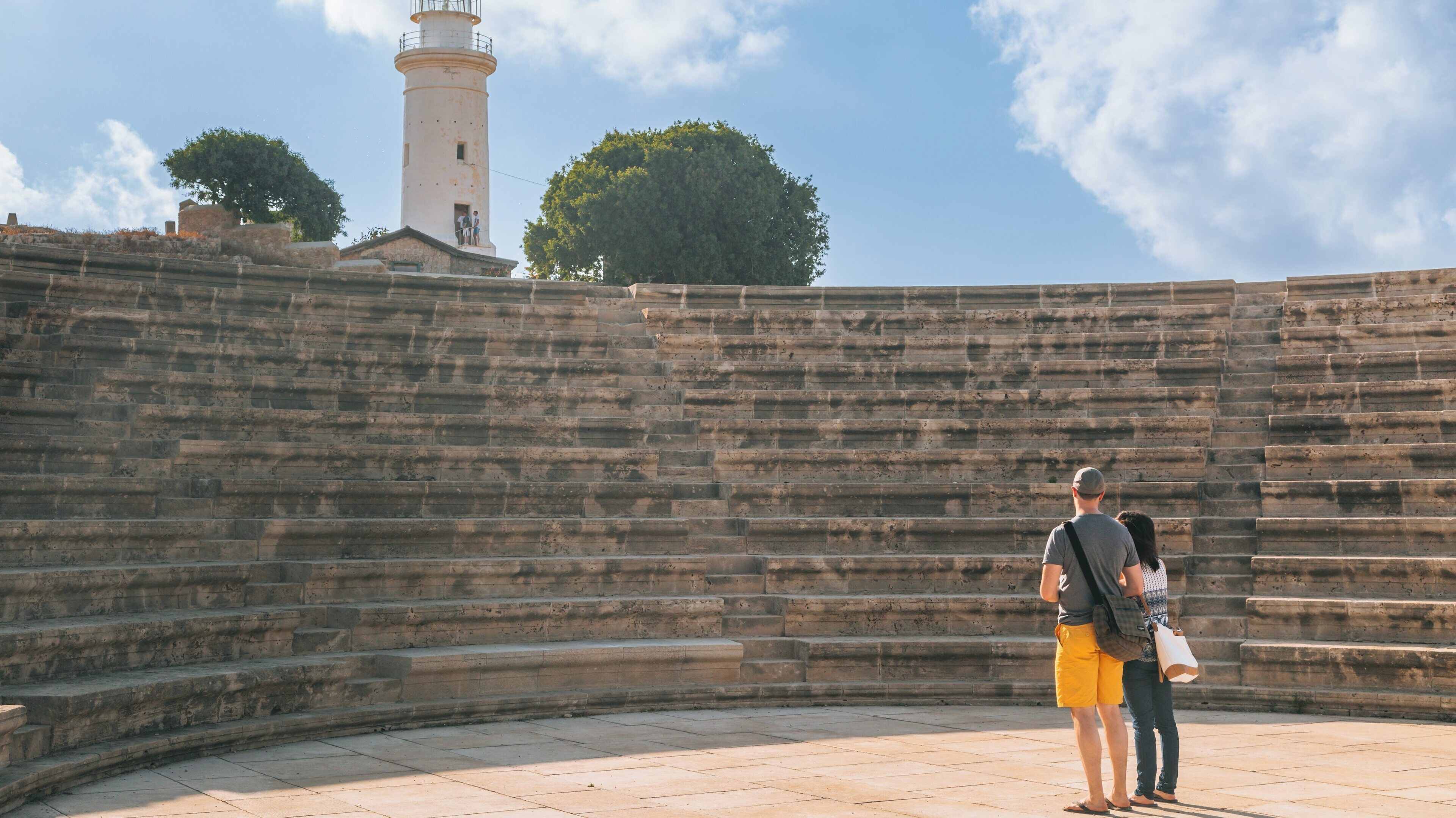 Visitors explore the ancient amphitheater at Paphos Archaeological Park in Cyprus under a bright blue sky