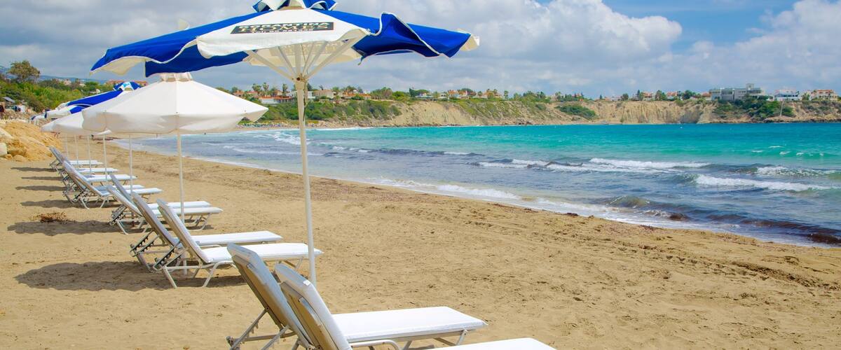 A beach with white lounge chairs and blue umbrellas.