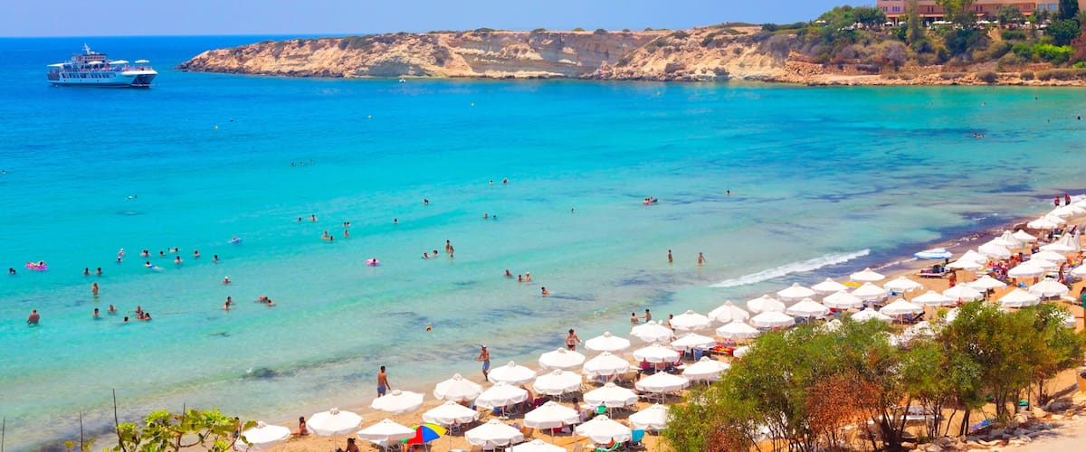 Uma praia com águas turquesa cristalinas, um cruzeiro e um edifício com telhados vermelhos.