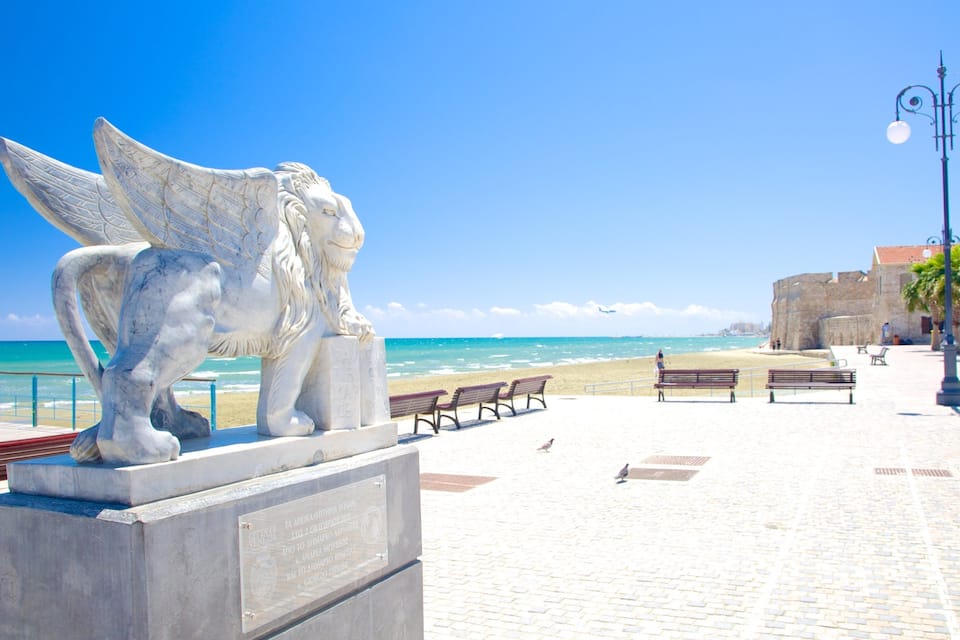 Estàtua de marbre blanc d'un àngel amb ales, una platja i una paret de pedra al fons.