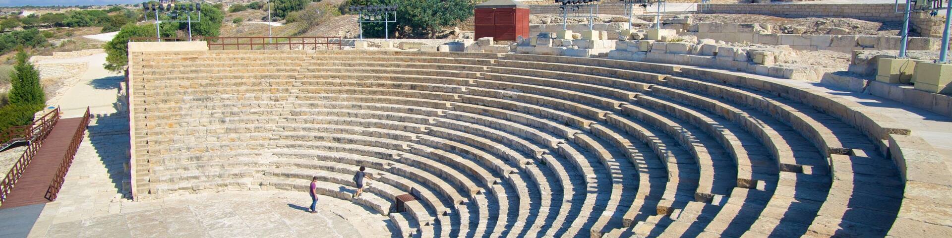 An ancient amphitheater with stone steps and a few people.