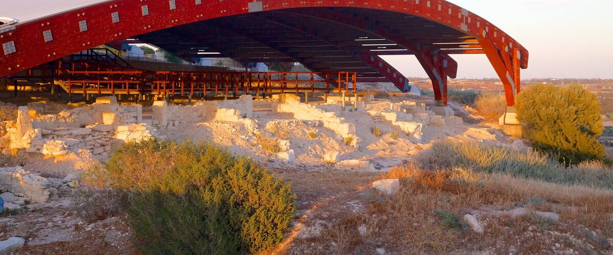 An ancient amphitheater with a red arch structure, ruins, and dry vegetation.