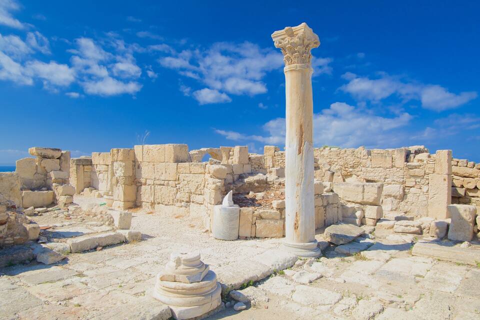 Ancient ruins with stone columns and scattered stone blocks under a clear blue sky.