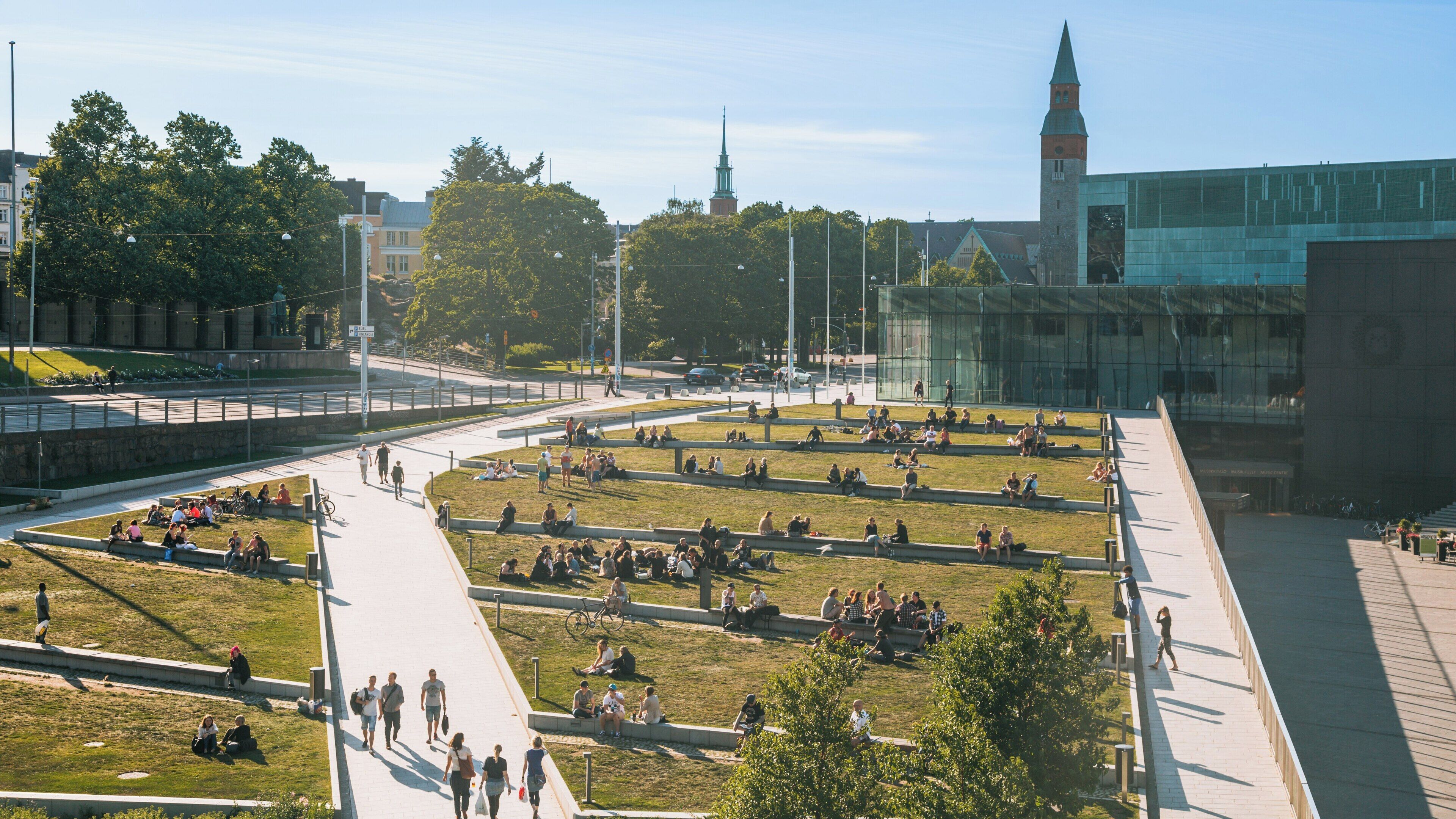 Visitors enjoy sunny day at Kiasma Museum of Contemporary Art in Helsinki, surrounded by art and greenery