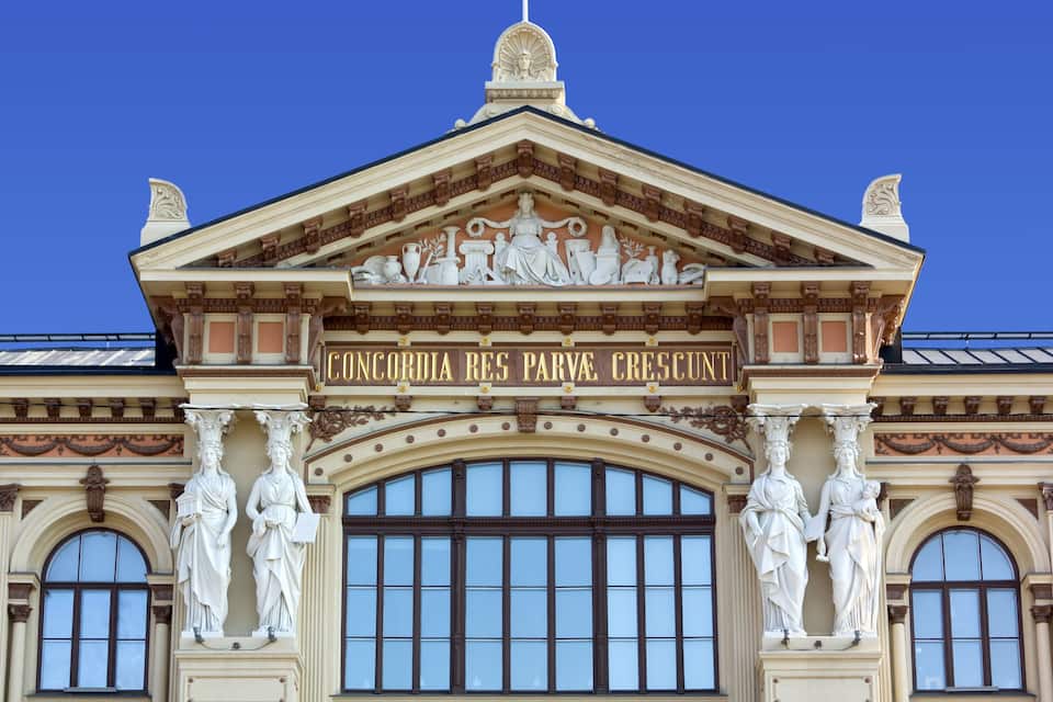 En klassisk bygningsfacade med detaljerede skulpturer og inskriptionen "CONCURSIA RES PARVA CRESCUNT".